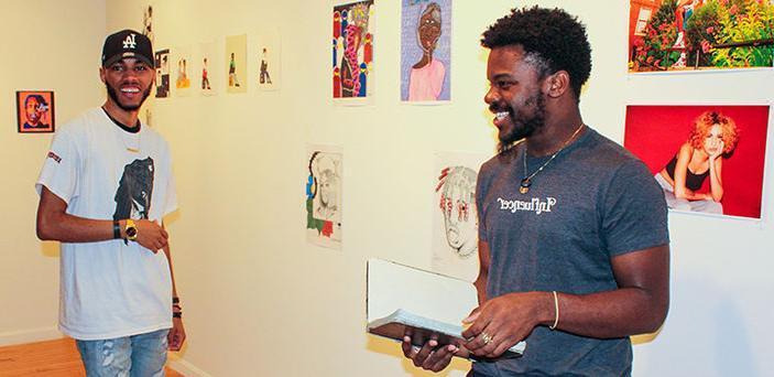 2 BSU students stand in front of their exhibits smiling in the Wallace Anderson Art Gallery on campus